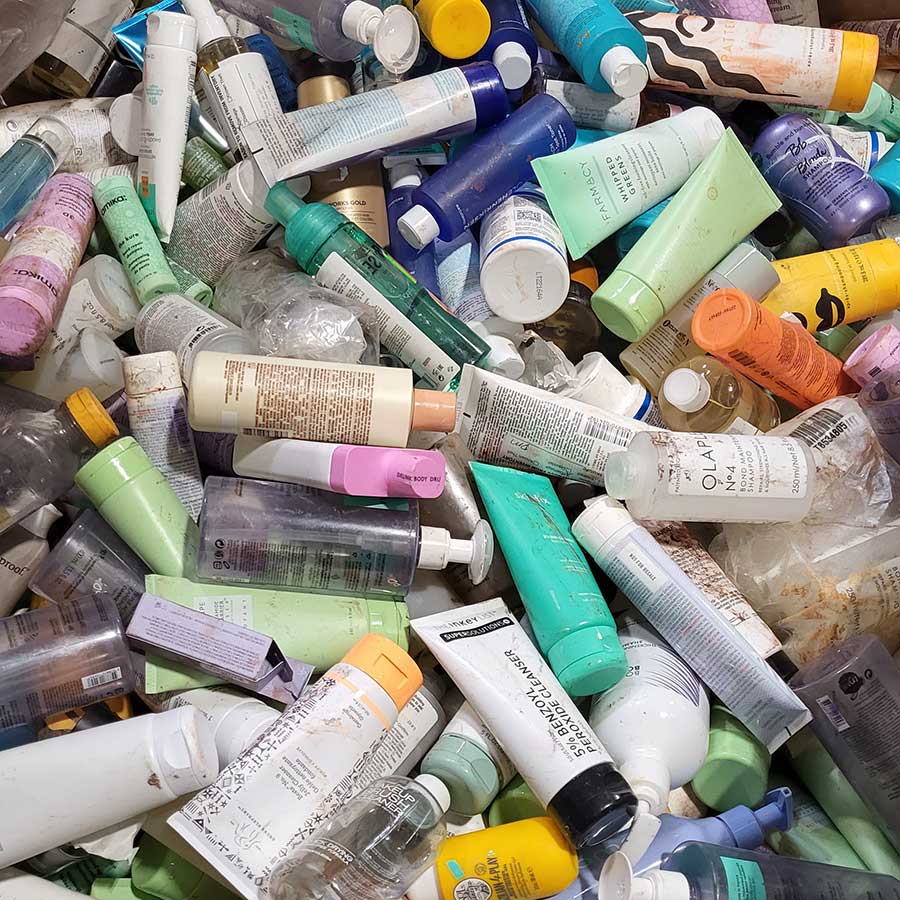 A large pile of assorted skincare and haircare bottles and tubes in various colors and sizes, many of them partially used or empty, scattered in a disorganized heap.